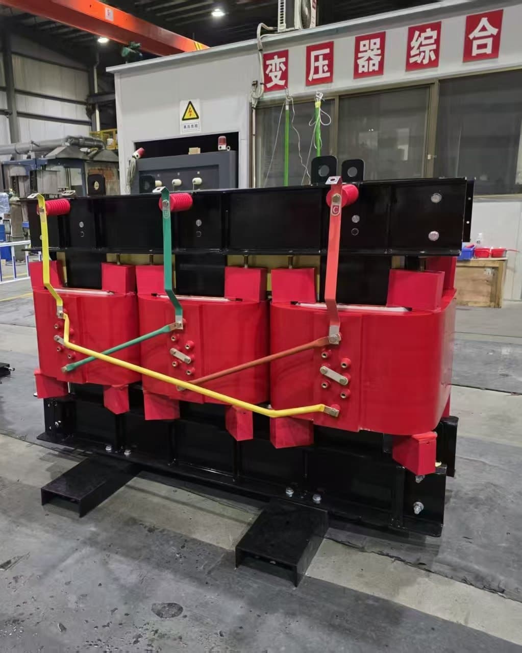 A cast resin transformer with red coils in front of the transformer test station in the factory hall