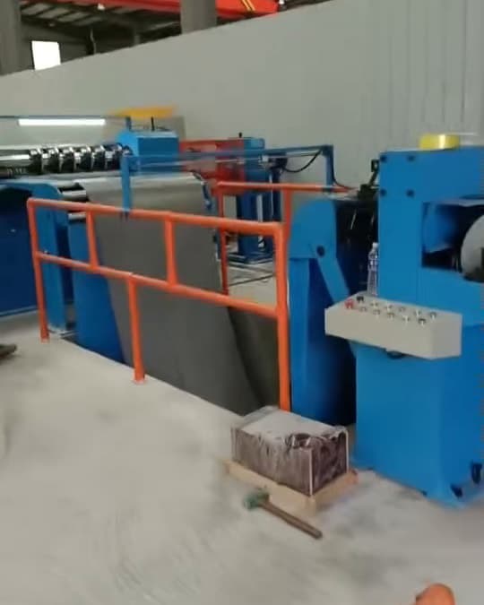 Blue slitting line cutting a coil of steel, with cut sheets stacked on a pallet beside it