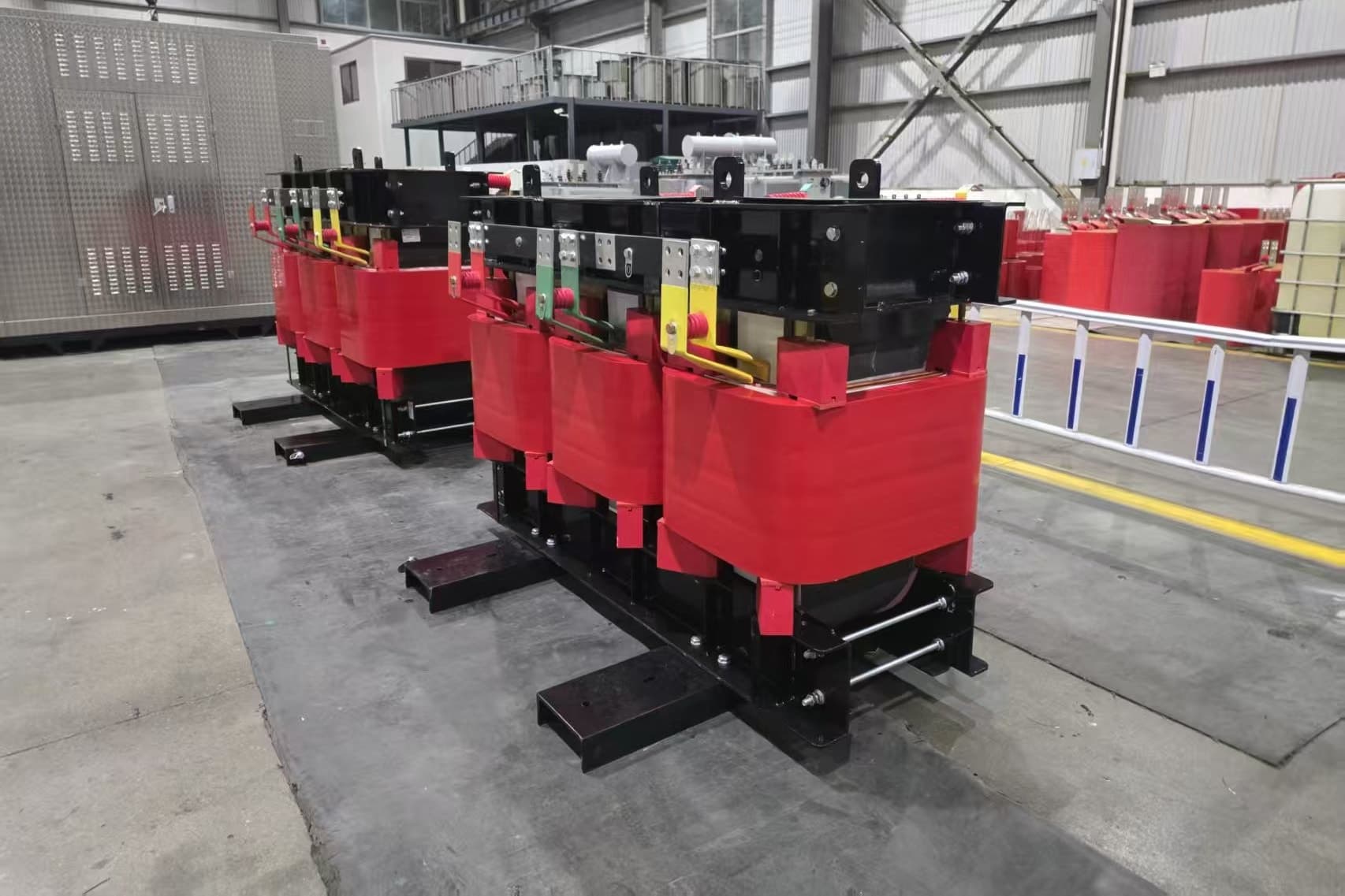 Two cast resin dry-type transformers with red coils standing on skids on the factory floor