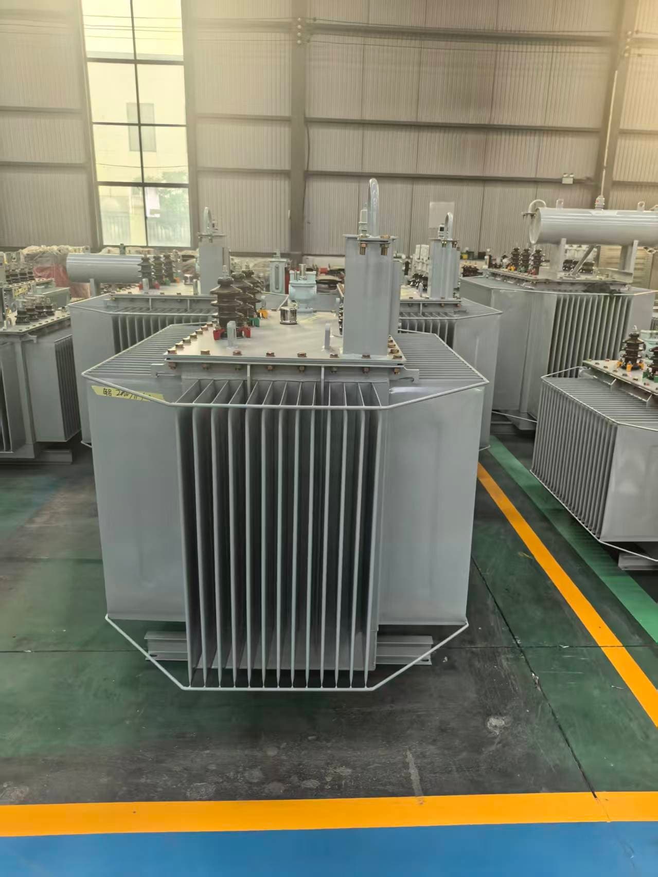 Oil-immersed transformer with a corrugated tank and a conservator, seen from the front on the factory floor