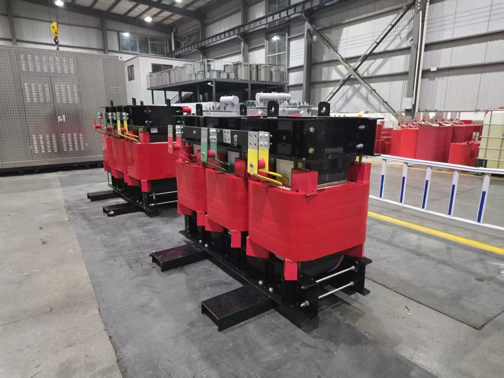 Two cast resin dry-type transformers with red coils standing on skids on the factory floor