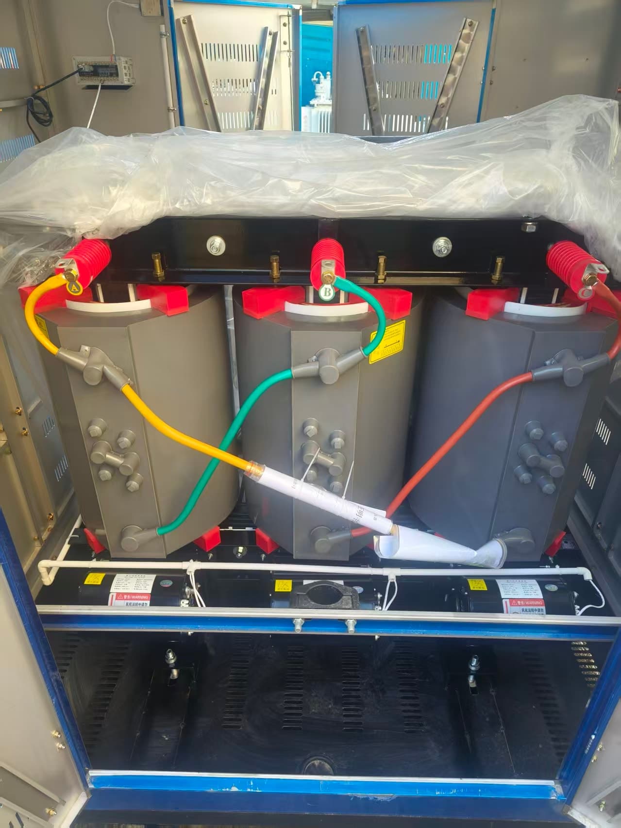 Cast resin transformer with grey coils inside a ventilated enclosure, partly wrapped in plastic